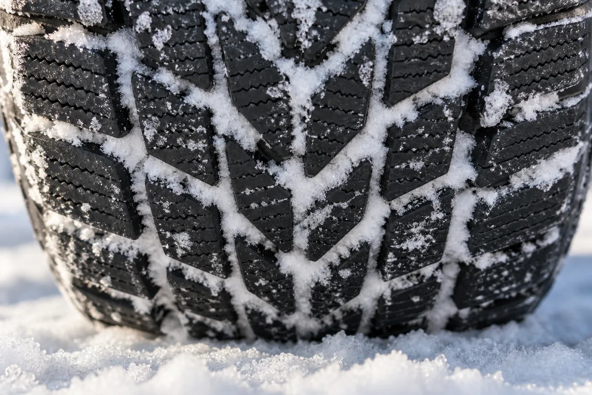 Gros plan sur la sculpture profonde d’un pneu, neige tassée dans les rainures