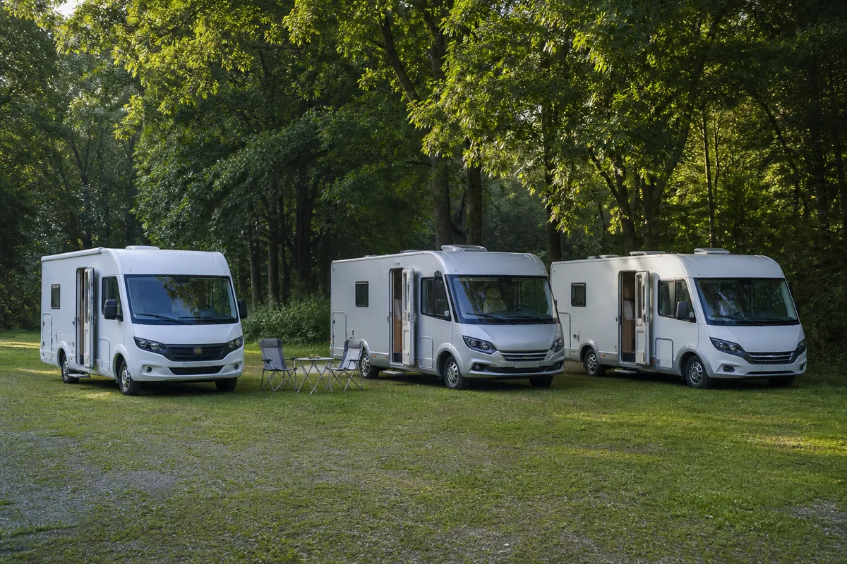 Trois camping-cars stationnés côte à côte sur une aire bordée d’arbres